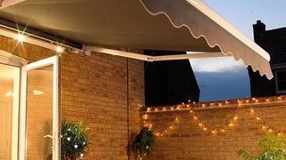 A grey awning hanging over a table set for dinner at nighttime, with fairy lights twinkling in the background