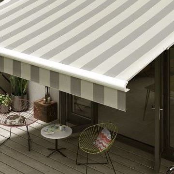 A grey-striped awning hanging over patio furniture on a bright day