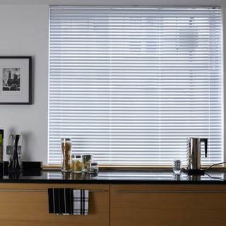 Light wood Portfolio Classic White Venetian blinds hung in a kitchen window