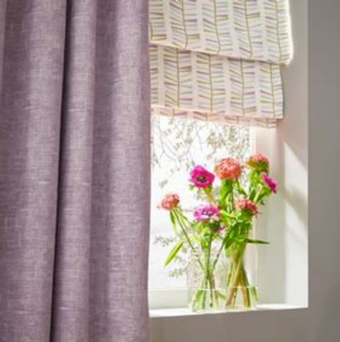 Purple shimmering curtains over cream printed roman blinds hanging on window