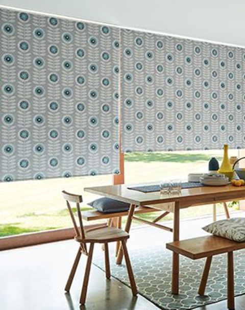 Dining room with a large table in front of floor to ceiling windows fitted with Neisha Teal Roller Blinds
