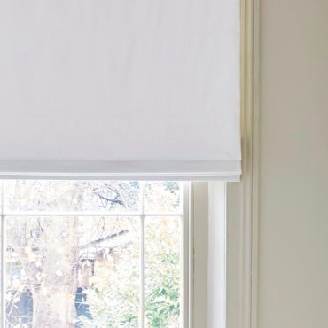white roman blinds with a view of a garden from a window