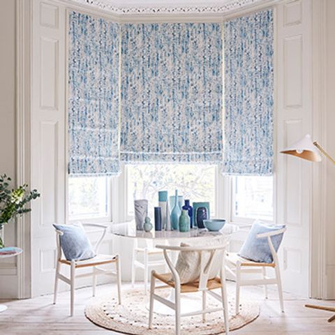 A table in front of a bay window with Mirage Ink Roman blinds fitted to the windows