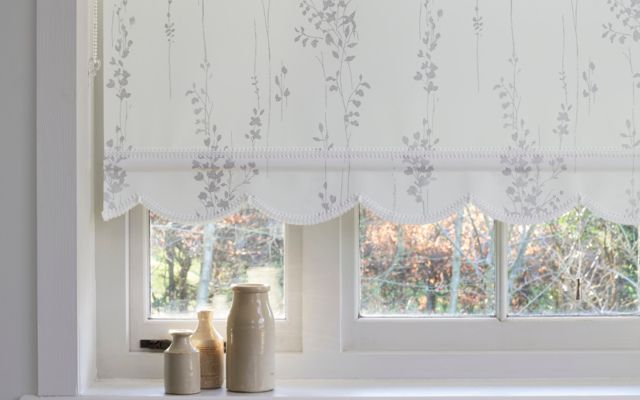 White roller blind fitted to a large window with a simple repeating leaf pattern in grey