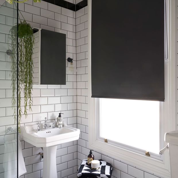 Black roller blind hung in bathroom with monochrome decor