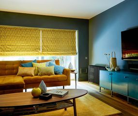 Retro style living room with blue and yellow decor and large windows dressed with yellow Roman blinds
