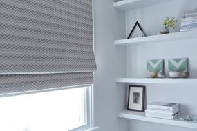 Minimal living room with white shelving and blackout Roman blinds