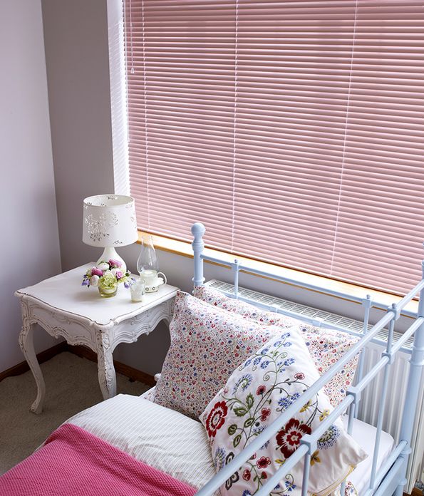 Close up of a child's bed and window covered in a pink Venetian blind