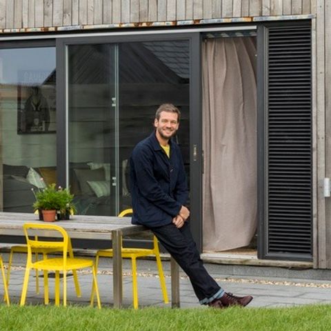 charlie luxton leaning on a yellow table in his garden with large patio windows in the background