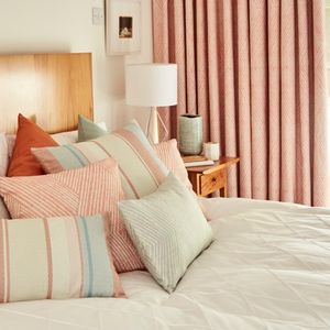 A bed dressed with custom cushions in Origami Persimmon fabric with matching curtains in the same fabric