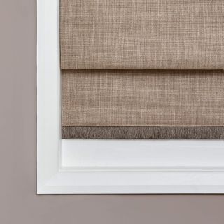 Sand coloured roman blind with brown fringing fitted to a window in a room with beige coloured walls