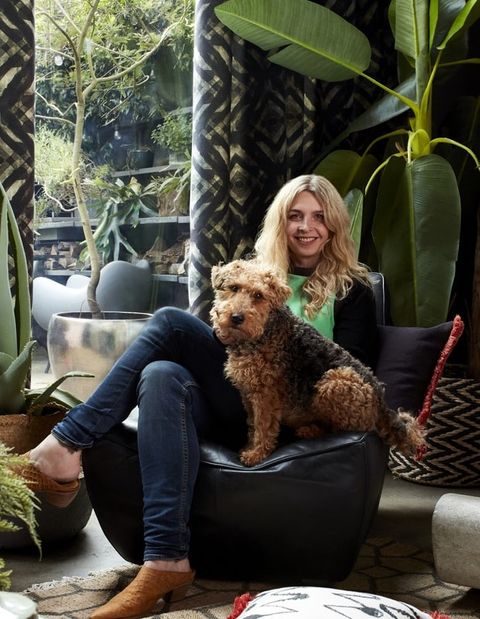 Abigail Ahern sat in a living decorated with geometrically styled curtains, plants and a dog sitting with her