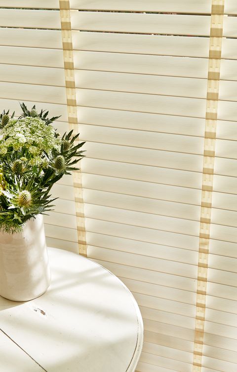 Close up of ivory wooden blinds with tape next to a side table with a vase of flowers