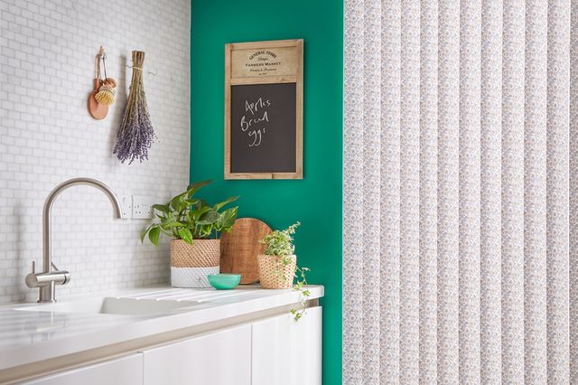 White vertical kitchen blinds fitted to a tall rectangular window in a kitchen decorated in white and green