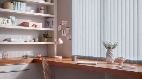 Modern home office with build in desk and shelves and windows dressed with pale blue vertical blinds