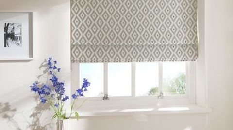 White and beige coloured roman blind designed with a repeating diamond and fitted to a rectangular shaped window in a room decorated in white