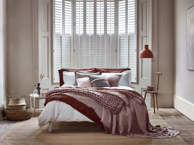 Tall tier-on-tier shutters covering a luxurious bedroom window. The shutters are white, with the louvres closed in the bottom half