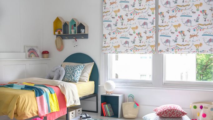 A children's bedroom featuring two windows that have a white blinds dotted with multi coloured circus animals