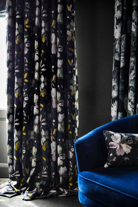 Close of up dark floral curtains in a living room. Matching floral print cushion have been placed on blue sofa