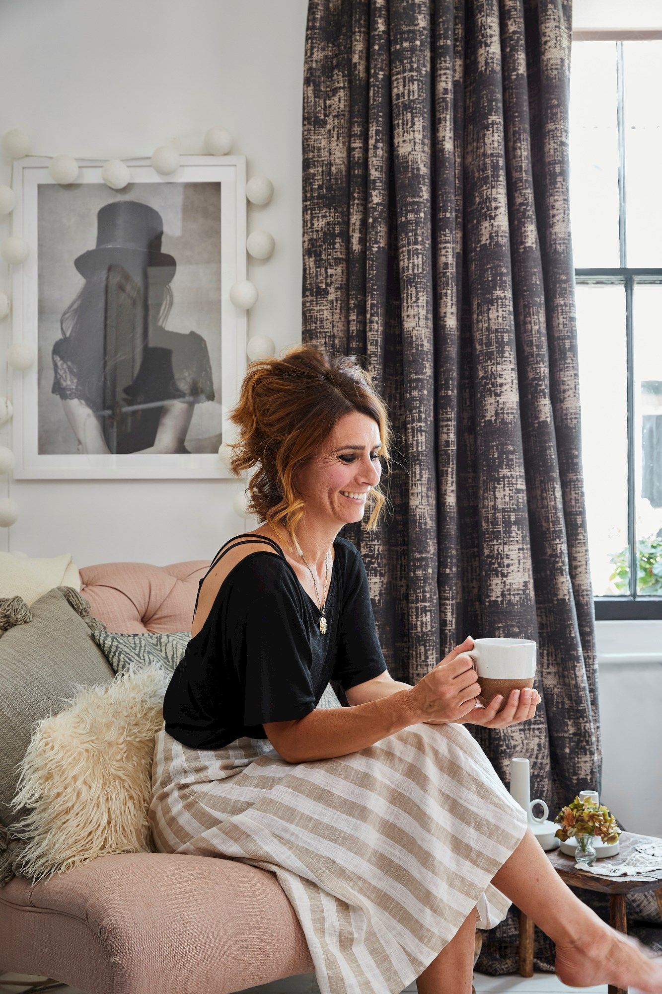 Instagram influencer Kyla Magrath sitting on a sofa in her living room next to window dressed in long dark curtains