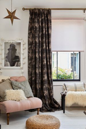 A black framed window with a textured grey curtain and pink Roller blind