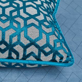 Shiny teal blue cushion with a repeating geometric pattern and light blue piped edge