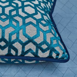Cushions decorated with shiny teal and grey geometric pattern along with a dark blue piped edge