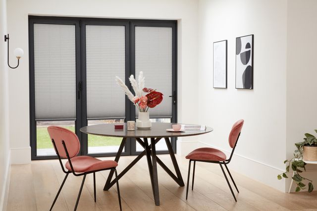 Grey Micro Pleat Pleated blinds dressed on bi-fold doors of dining room. Round table along with pink chairs have been placed in the room.