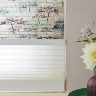 Close up of light grey Transition Pleated binds featuring some trees printed with dots in turquoise or purple on top blind and sheer white blind underneath.