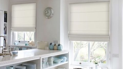 Ivory coloured roman blinds attached to rectangular windows in a kitchen decorated in white with marble countertops