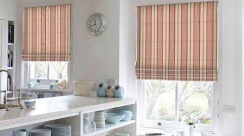 Two pink and white striped roman blinds attached to rectangular windows in a kitchen decorated in white