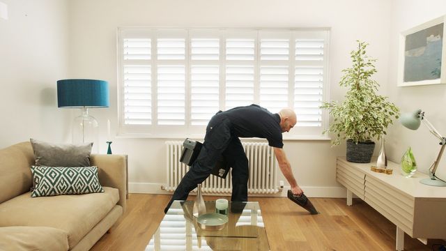 Advisor vacuuming floor and picking up toolbox in lounge with shutters
