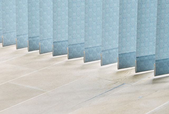 Soft blue coloured vertical blinds nearly touching a stone floor