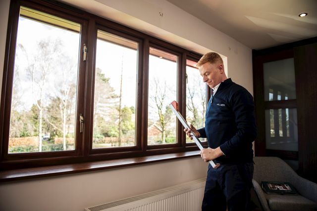 An advisor measuring for blinds across a series of four wooden blinds