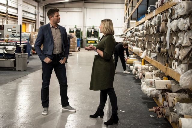 Somebody talking to a member of the product team in a hillarys warehouse which has rolls of fabric stacked onto the shelves