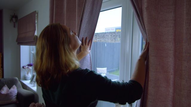 Customer pulling back pink curtains in new build home