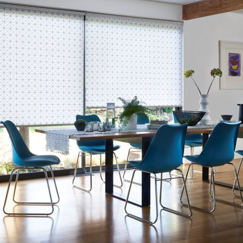 Cosmic Jet white and blue roller blinds in a wide window behind a dining table with blue chairs
