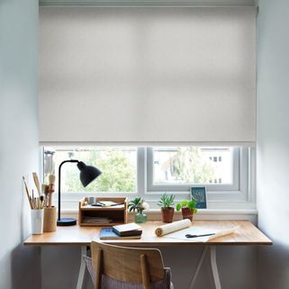 A small office space with the Harrow Glacier Roller blind freely hanging in a window above the desk. The printed design is set against neutrally decorated walls.