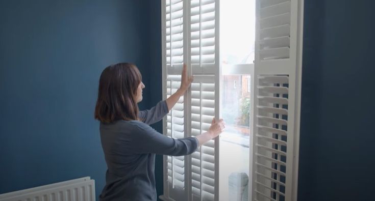 image of lady adjusting white shutters fitted to a white window in a blue room