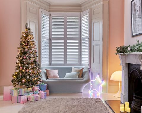 White shutters in a living room with a sofa facing away from the windows. A fireplace on the right side and a christmas tree next to the sofa. A light up star ornament is next to the sofa.
