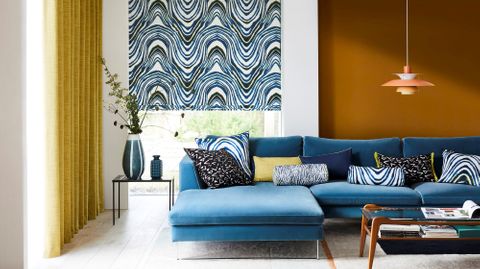 Blue and white patterned roman blind fitted to a window in a living room along with a yellow floor to ceiling curtain