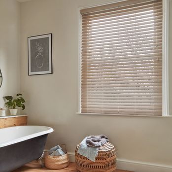 light oak faux wood blinds in bathroom window next to a bathtub, laundry basket