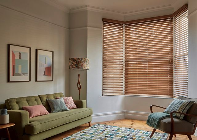 Mirage Rich Oak Blind at a bay window in a living room with a green sofa to the left and a small chair to the right