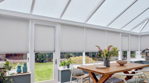 crush silver grey conservatory pleated blinds by a wooden dining table and numerous plants
