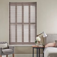 weathered grey shutters in a bedroom inbetween a grey chair and bed on an off white wall