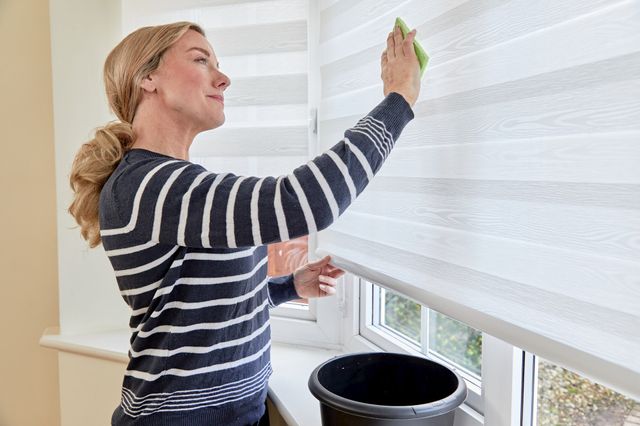 woman cleaning white day & night roller blinds with green sponge