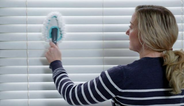 woman cleaning white wooden blinds