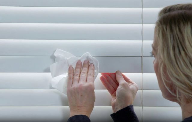 woman wiping white wooden blinds