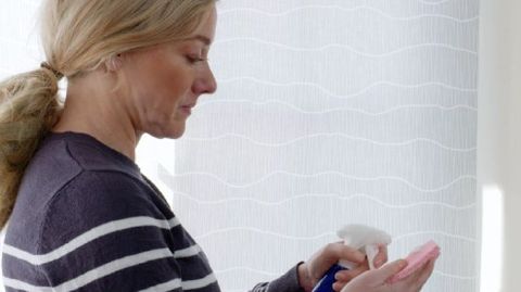 lady with blonde hair using cleaner spray on a sponge ready to clean roller blind