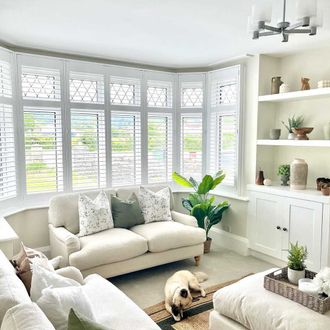 Full height white shutters on a bay window in a cream living room with dog lying on floor
